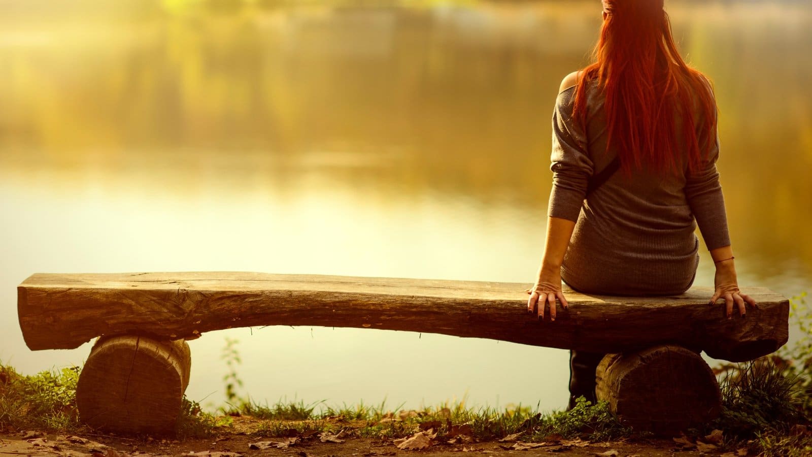 Women by herself sitting on a bench looking out over a lake contemplating.